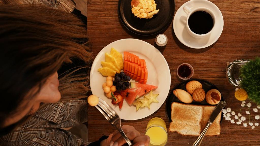 Mesa con frutas tropicales, café, jugo, huevos y pan en presentación colorida