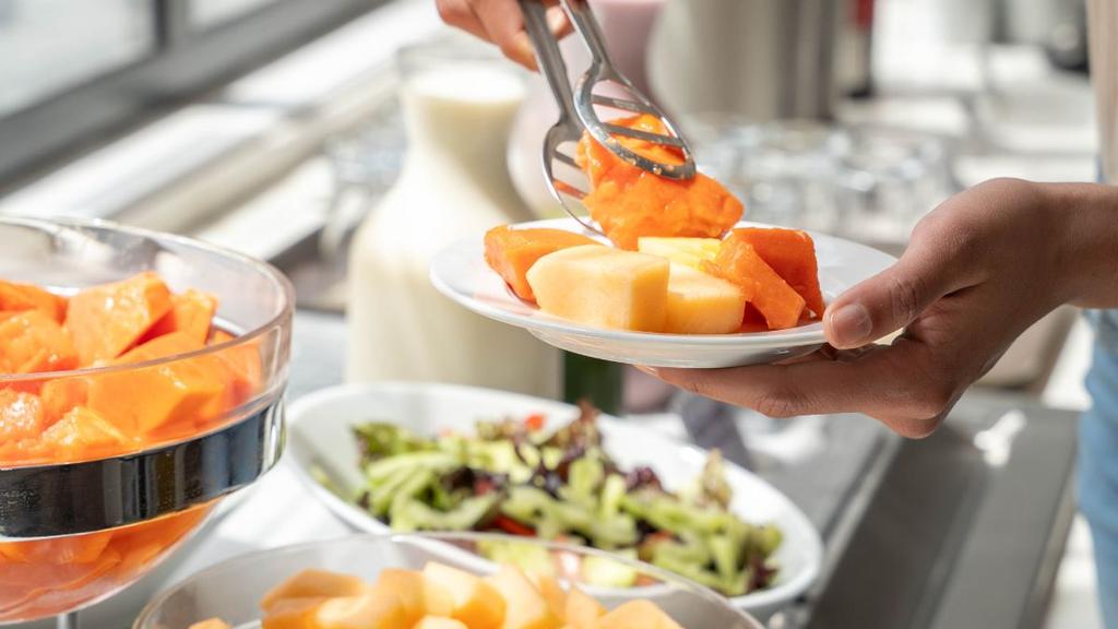 Frutas cortadas servidas con pinzas en plato blanco en zona de buffet